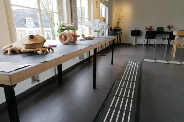 Tijdelijke geleideroute van matten en klankplaten in een expositieruimte met tastbare kunstwerken.